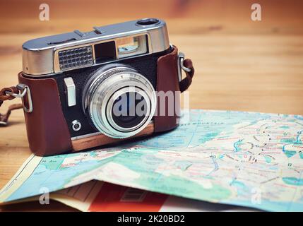 Tempo di andare a vedere le attrazioni turistiche e catturarle. Primo piano di una macchina fotografica antiquata e di una mappa giacente su un tavolo di legno. Foto Stock