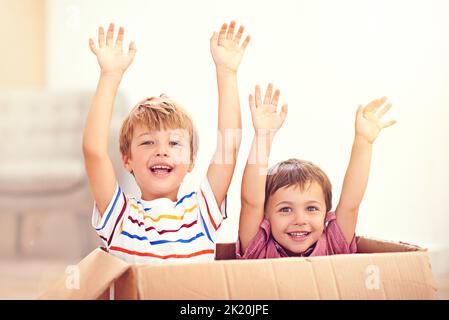 Siamo arrivati al sicuro. Due giovani fratelli alzano le braccia mentre saltano fuori da una scatola di cartone. Foto Stock