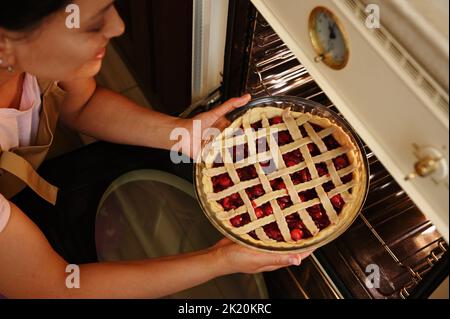 Primo piano di una bella donna sorridente torta di cottura, mettendola nel forno caldo nella cucina di casa Foto Stock