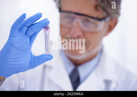 Apparecchiature fondamentali per il laboratorio. Un tiro corto di uno scienziato maturo che guarda una provetta nel suo laboratorio. Foto Stock