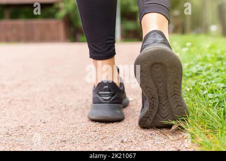 Primo piano delle gambe di una donna, in sneakers nere , camminando lungo un sentiero fatto di piccola pietra rossa Foto Stock