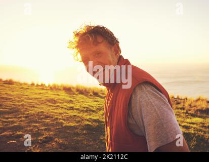 Amare il tempo lontano dalla città. Ritratto di un uomo in piedi su una collina al tramonto con l'oceano sullo sfondo. Foto Stock