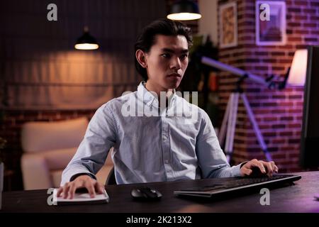 Freelance maschile che lavora a distanza sul computer, frequentando lezioni online a casa. Lavorare in remoto su report aziendali con piano dati di ricerca e informazioni, inviando e-mail sul sito Web. Foto Stock