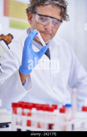 Una cura è in arrivo. Un tiro corto di uno scienziato maturo che guarda una provetta nel suo laboratorio. Foto Stock