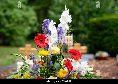fiori colorati come sistemazione in tomba dopo un funerale di fronte a croci di legno in sfondo sfocato Foto Stock