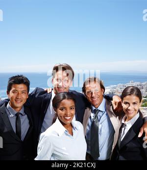 Formare nuovi legami nell'aria fresca. Foto di gruppo di gente sorridente d'affari con una città costiera sullo sfondo. Foto Stock