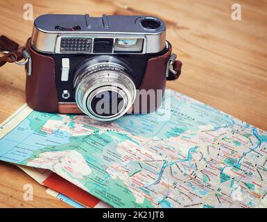 Esplorazione delle vacanze. Primo piano di una macchina fotografica antiquata e di una mappa giacente su un tavolo di legno. Foto Stock