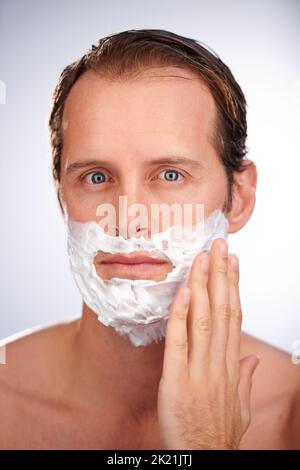 I suoi stoppie in difficoltà. Studio shot di un bell'uomo che applica la crema da barba. Foto Stock