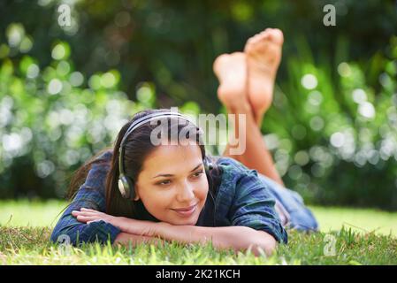 Una giovane donna allettante, stesa sull'erba e che ascolta musica. Foto Stock