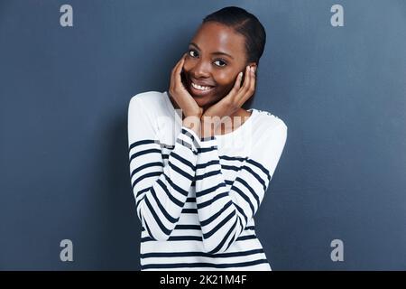 Tu mi appiattire. Ritratto di una giovane donna attraente in piedi con la testa in mano su uno sfondo grigio. Foto Stock