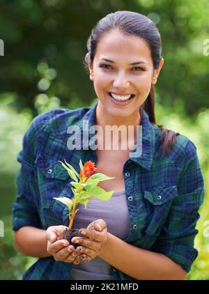 Divertirsi in giardino. Ritratto di una giovane donna attraente che tiene una pianta giovane. Foto Stock