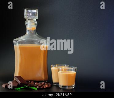 Liquore alla crema di cioccolato, alcol fatto in casa su sfondo nero, accanto a pezzi di cioccolato, foglie di menta e chicchi di caffè. Primo piano. Foto Stock