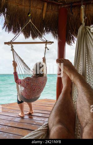 Donna su una sedia di corda sotto un tetto di paglia che guarda verso l'acqua alla laguna di Bacalar in Messico Foto Stock