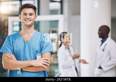 Ritratto di un'infermiera maschile con il suo team sullo sfondo dell'ospedale. Infermiere felice, sorridente e fiducioso con medici in medicina, salute e. Foto Stock