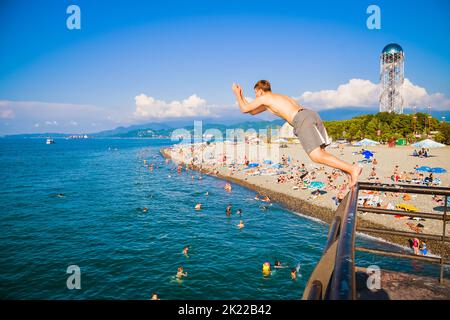 Batumi, Georgia - 4th agosto, 2022: maschio caucasico turistico salto in acqua di mare dal molo di Batumi in caldo giorno d'estate. Vacanza sulla costa del Mar Nero i Foto Stock