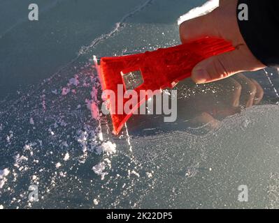 la mano rimuove il parabrezza ghiacciato di un'auto con un raschietto di ghiaccio al mattino presto, primo piano Foto Stock