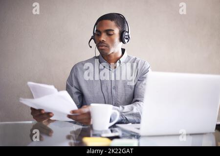 HES ha avuto accesso a tutti i file client. Un giovane uomo d'affari che indossa una cuffia che passa attraverso alcuni documenti al suo laptop. Foto Stock