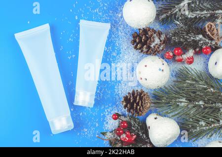 Tubi color crema e decorazioni natalizie. Imballo mockup di idratante su un tavolo innevato con coni di pino, rami di albero e palle di neve Foto Stock