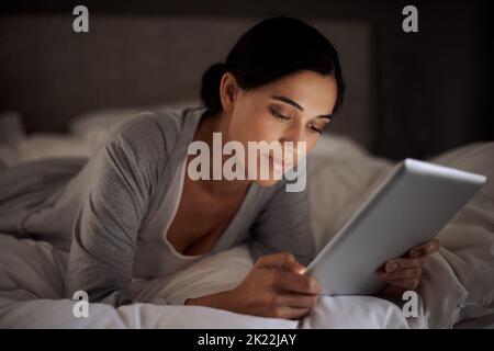 Prima di andare a letto, una giovane donna attraente che usa il suo tablet a letto. Foto Stock