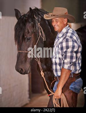 Il suo tempo di andare per un giro. Una mano di ranch di cura che si prende cura di un cavallo nella stalla. Foto Stock