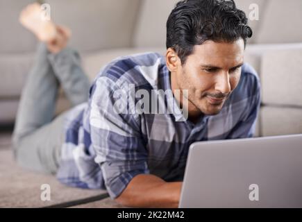 HES profondamente immerso nel mondo del web. Un giovane uomo che usa il suo notebook a casa. Foto Stock