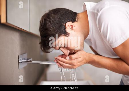 Ripulendo via il sonno delle notti precedenti, un giovane si lava il viso nel lavandino del bagno. Foto Stock