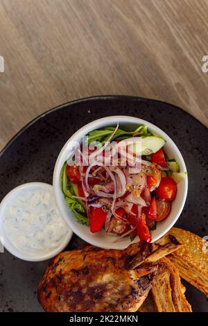 Pollo arrosto o anatra in verticale delizioso e succoso con insalata di verdure di cetrioli, pomodoro, cipolla, panini dolci sul tavolo Foto Stock