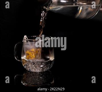 Un primo piano di una teiera che versa l'acqua bollente in un bicchiere con il tè Foto Stock