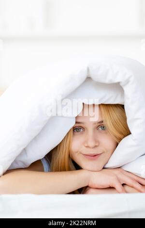 Mattina accogliente. Weekend pigro. Riposo benessere. Comfort della camera da letto. Ritratto di tranquilla giovane sorridente bella donna sdraiata a letto sotto soffice e pulita cedshe bianca Foto Stock