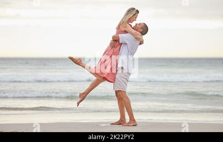 Coppia interrazziale, amore e abbracciare su una spiaggia in riva al mare in vacanza in natura. L'uomo e la donna nell'affetto gioioso di rapporto insieme vicino Foto Stock