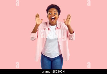 La donna afro-americana overjoyed urla WoW vedendo la sorpresa inaspettata si leva su sfondo rosa Foto Stock