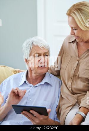 È un problema che si ripresenta: Una coppia felice di anziani che utilizza un tablet digitale a casa. Foto Stock