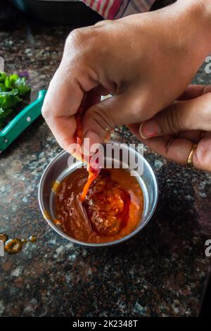 Persona che versa la salsa di peperoncino rosso caldo in una ciotola in una cucina domestica indiana. India. Foto Stock