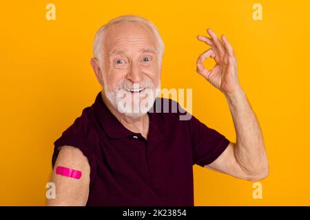 Foto dell'uomo anziano mostra le dita simbolo di okey promo vaccinato clinica perfetta isolata su sfondo di colore giallo Foto Stock