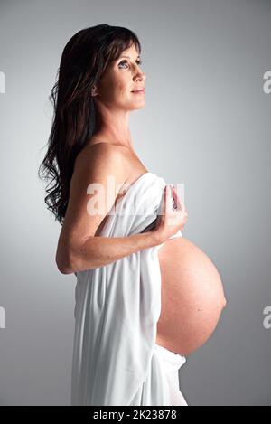 Aspettandosi il suo arrivo presto. Una donna incinta che tiene la pancia. Foto Stock