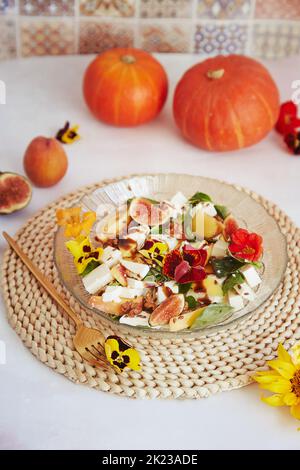 Insalata vegetariana fresca autunnale con fiori commestibili, fichi, pesche, verdi e feta su sfondo in ceramica con decorazioni in zucca autunnale Foto Stock