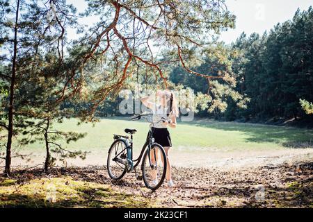 Benefici per la salute mentale del ciclismo, ridurre l'ansia. Ciclismo nella foresta. Piste ciclabili della foresta. Donna singola in bicicletta in pineta nelle giornate di sole. Foto Stock
