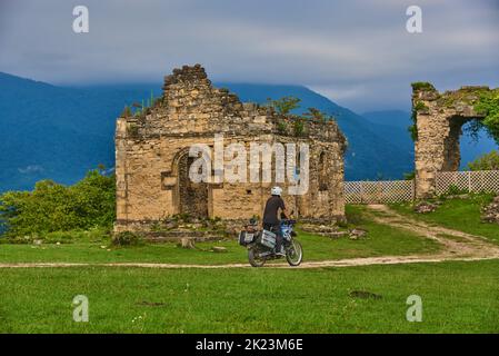 Un uomo in moto percorre una strada sterrata tra erba verde fino alle rovine di un antico tempio di Bedia. Foto Stock