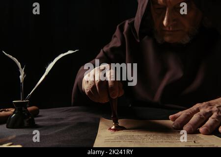 monaco medioevale in vestibolo scuro con pergamena di stampaggio cappuccio con sigillo di cera isolato su nero, immagine stock Foto Stock