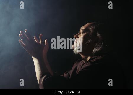 vista laterale del prete medievale che prega su sfondo nero con fumo, immagine stock Foto Stock