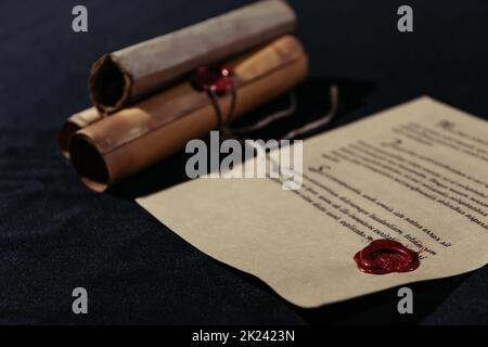 vecchio manoscritto stampato con sigillo di cera vicino a pergamene arrotolate su sfondo nero, immagine stock Foto Stock