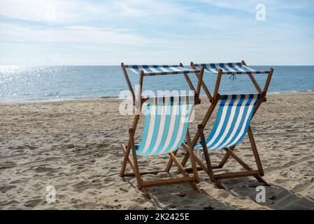 Coppia di sedie a sdraio a righe blu e bianche su una spiaggia di sabbia con nient'altro che oceano aperto in lontananza. Foto Stock