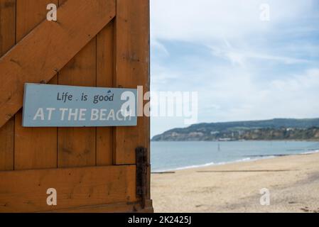 La vita è buona al cartello spiaggia su una porta con una spiaggia fuori fuoco dietro di essa. Foto Stock