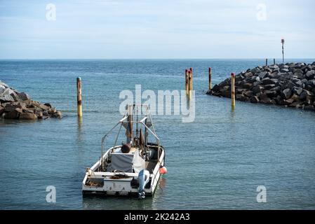 La barca ormeggiata vicino all'entrata di un piccolo porto sull'Isola di Wight, Inghilterra. Grandi massi su entrambi i lati come parte delle difese marine. Foto Stock