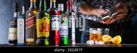 POZNAN, POL - DEC 28, 2021: Bottiglie di vari marchi internazionali di liquori duri e barman preparare una bevanda con un cocktail shaker Foto Stock