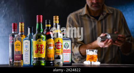 POZNAN, POL - DEC 28, 2021: Bottiglie di vari marchi internazionali di liquori duri e barman preparare una bevanda con un cocktail shaker Foto Stock