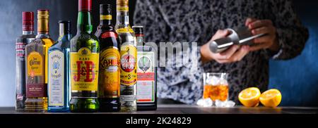 POZNAN, POL - DEC 28, 2021: Bottiglie di vari marchi internazionali di liquori duri e barman preparare una bevanda con un cocktail shaker Foto Stock