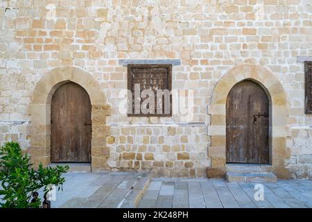 Due porte intemperate in legno ad arco e una finestra chiusa in ferro battuto arrugginito su mattoni parete in pietra e pavimento in piastrelle di pietra Foto Stock