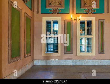 Parete arancione ad angolo con due finestre in legno con persiane verdi, belle ed eleganti cornici verdi rettangolari con contorno ornato e marmo bianco piastrellato Foto Stock