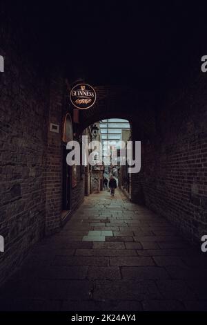 Un vicolo nel centro di Dublino che conduce ad un invitante buco di irrigazione con un iconico logo Guinness su un cartello. Foto Stock